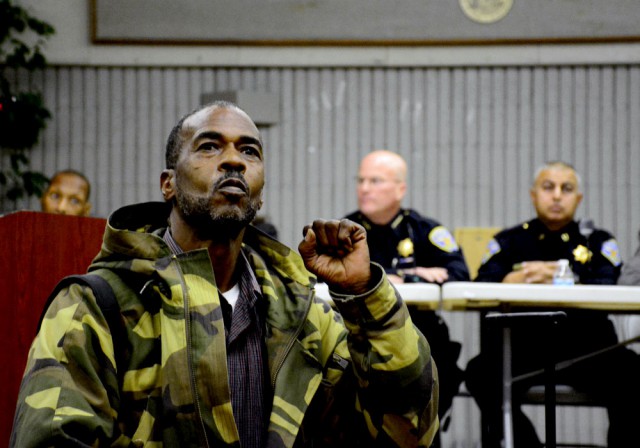 A community member by the name of Kilo G holds up a fist in front of a panel of SFPD members including Police Chief Greg Suhr during a community forum regarding the death of Mario Woods.