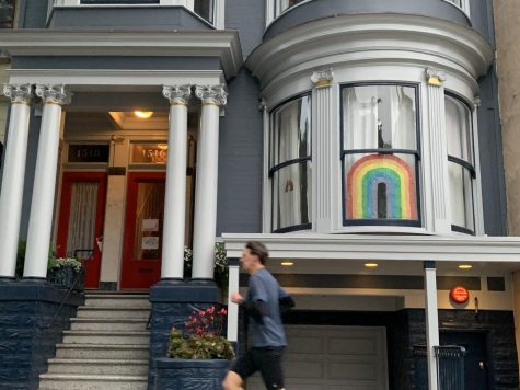 A lone runner jogs past a large rainbow near Haight St. 
