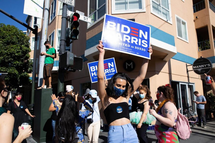 Jupiter Peraza waves a Biden-Harris 2020 sign outside of her work, Manny’s, which held one of San Francisco’s many Biden block parties on the corner of 16th St. and Valencia Ave. on Saturday, Nov. 7, 2020. (Saylor Nedelman / Xpress Magazine)
