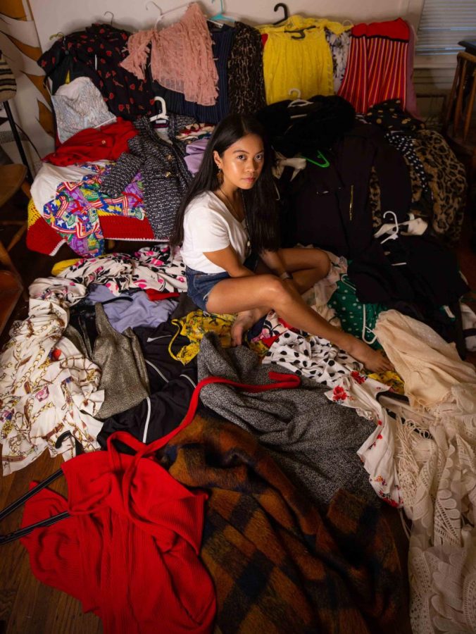 Carla Bayona poses with all of her clothes that contain a label listing fossil-fuel-derived fabrics in her San Francisco apartment on Oct 3, 2021. Polyester, polyamide, elastane, acrylic, and polypropylene are the most common fossil-fuel-derived textiles found in everyday clothing. (Saskia Hatvany / Xpress Magazine)