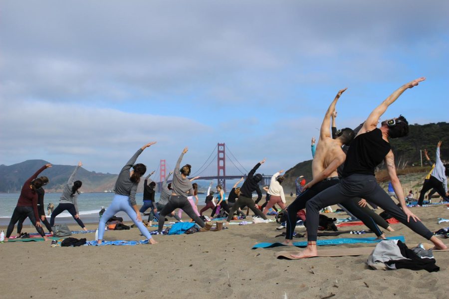 The yoga class gets instructed to do the peaceful warrior pose at Baker Beach in San Francisco on Dec. 4, 2021. (Paris Galarza / Xpress Magazine)