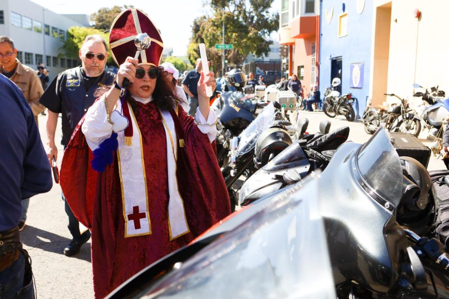 Miriam Moody, dressed as a bishop, blesses
the bikes lined up outside of the San Francisco Motorcycle Clubhouse. Moody spent two years around the club before prospecting in
2019. She had her official initiation on this day, due to the pandemic disrupting the regular club initiation during her initial prospecting
period. (Gina Castro / Xpress Magazine)