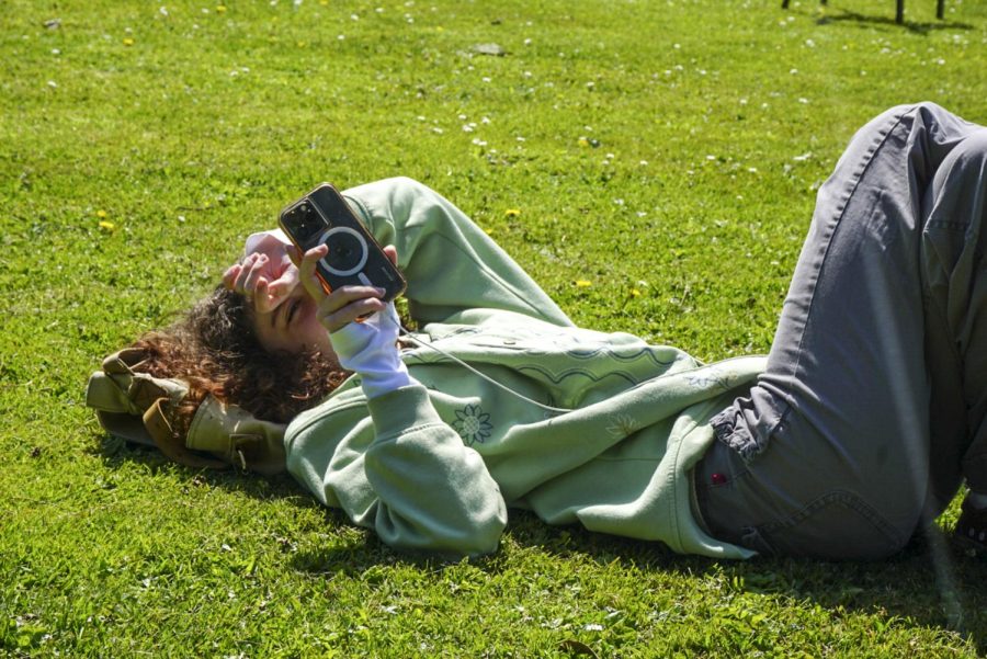 A SF State student facetimes her friend while laying on the grass of the quad after a long day of classes in San Francisco, Calif., on April 5, 2023. (Tatyana Ekmekjian / Xpress Magazine)