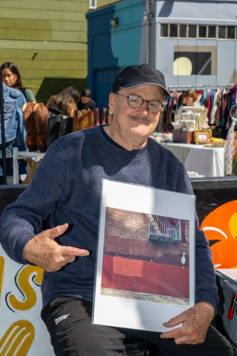 Local street photographer, J.B. Higgins, poses for a photo with one of his street photographs he took at the corner of Valencia and 18th Street in San Francisco, California on September 3, 2023. (Ryo Kojima/Xpress Magazine)