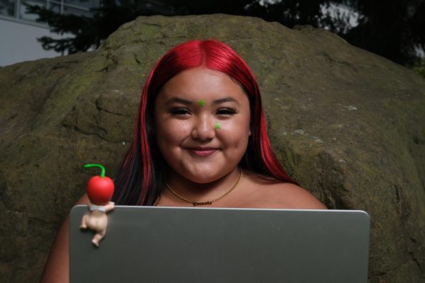 Gisselle Peñuela Solis poses for a portrait using her laptop, which has a sonny angelclimbing on the back, in between Burke hall and the fine arts building on Monday, October 2, 2023. (Andrew Fogel/Xpress Magazine)