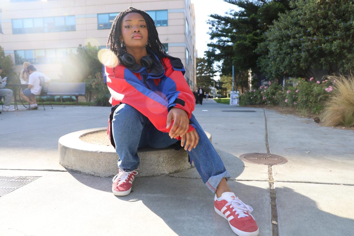 Wearing+a+blue+and+red+windbreaker+jacket%2C+white+cropped+tank+top%2C+blue+jeans%2C+and+red+Adida+sneakers%2C+Luna+Fife+poses+for+a+portrait+in+front+of+SF+State%E2%80%99s+Humanities+building.++
