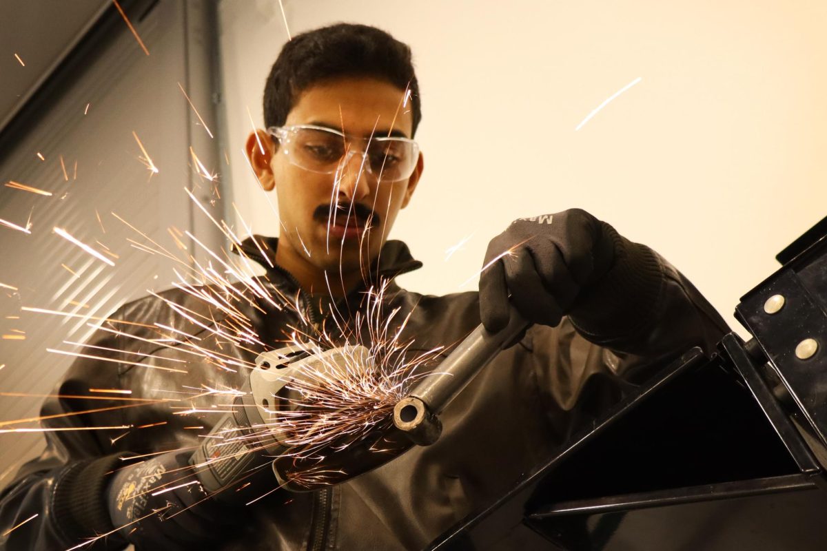 Hashem Mishal using an angle grinder to cut a drill bit, in the SAE team’s garage at SF State on Tuesday, Nov. 12, 2024. “We don't get anything from the school other than this workshop,” Mishal said. “Our advisor, he runs the shop, and he also works with us to try and get as [many] opportunities as possible. So it was really nice, in helping us get this space, but all the tools are just some of the guys’ or third parties’. I don't know where these tools came from, but a lot of it was sponsors, donations from alumni. Right now, all the hardware we’ve been paying out of pocket for the time being.”  (Jonah Chambliss / Xpress Magazine)